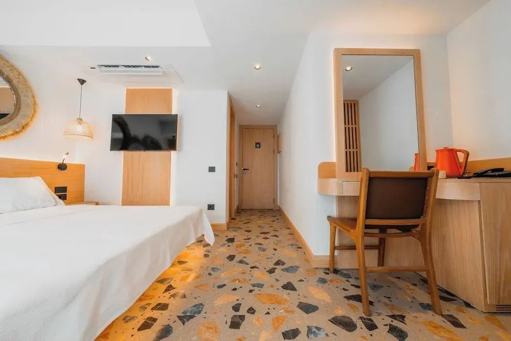 Modernes Hotelzimmer mit gemustertem Terrazzoboden, Fernseher und Schreibtisch mit Holzstuhl.