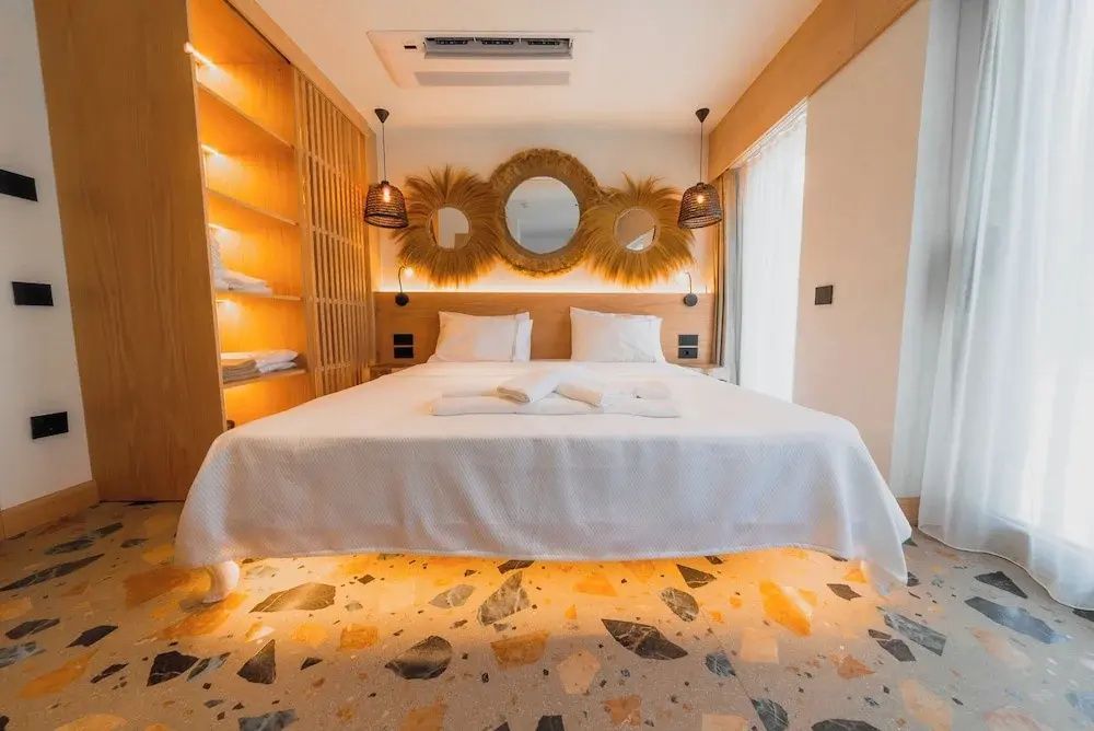 Doppelbett mit weißer Bettwäsche, indirekter Beleuchtung und Terrazzoboden.