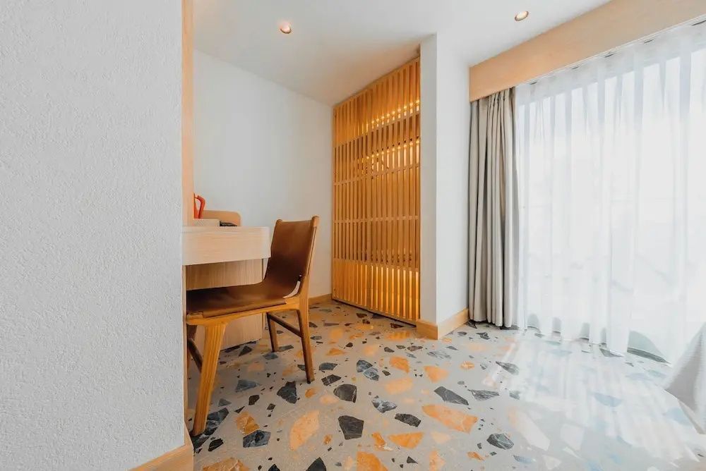 Schreibtisch aus Holz mit Stuhl und Holzschrank auf buntem Terrazzoboden im Zimmer.