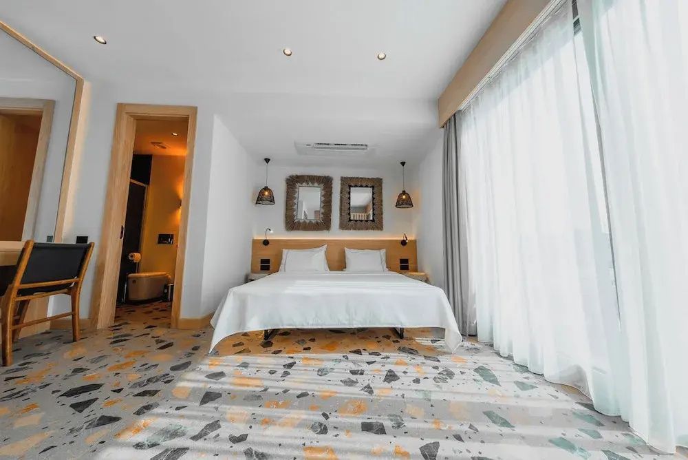 Hell eingerichtetes Doppelzimmer mit weißem Bett, Spiegeln an der Wand und buntem Terrazzoboden.