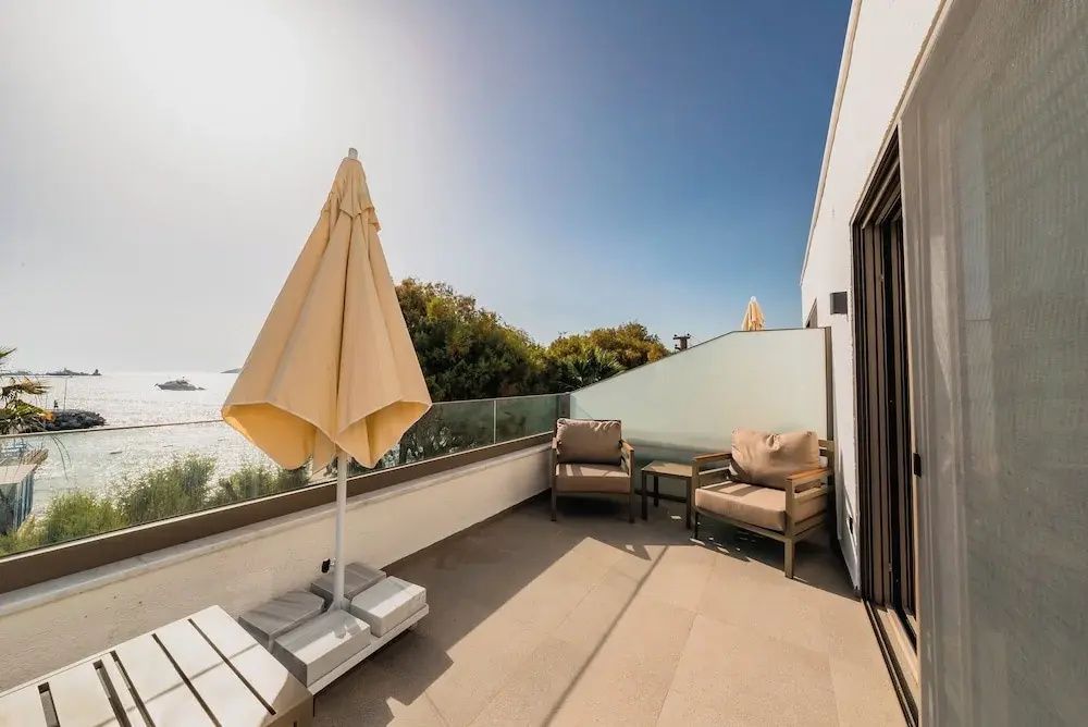 Terrasse mit zwei Sesseln, Beistelltisch und geschlossenem Sonnenschirm.