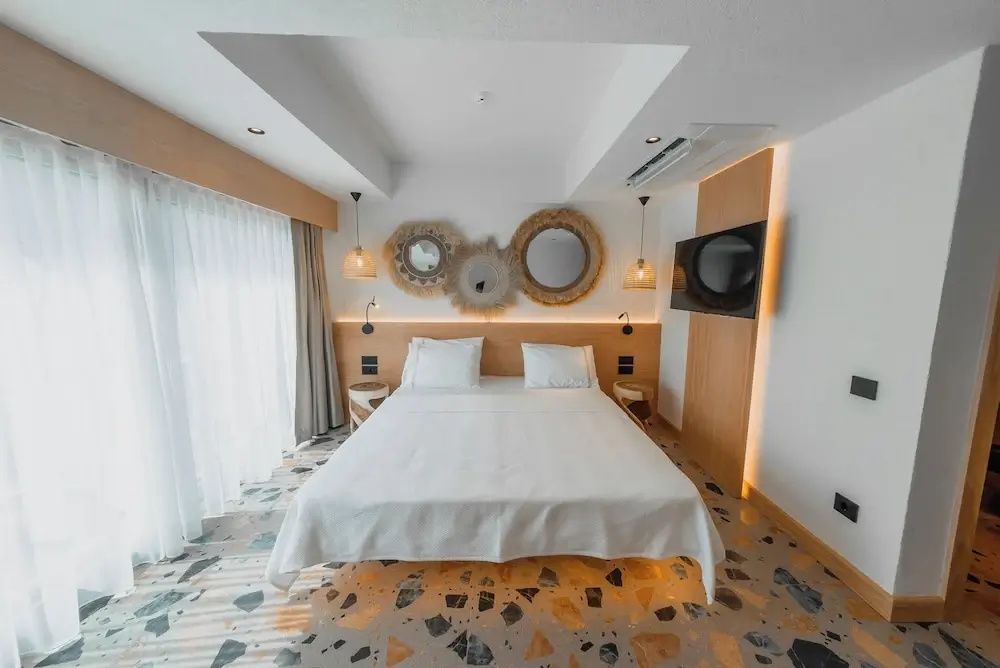 Doppelbett im Hotelzimmer mit Wand TV, Terrazzoboden und rundem Spiegelschmuck an der Wand.