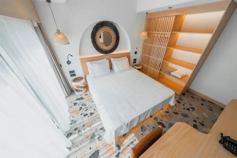 Blick von oben auf ein gemachtes Doppelbett mit rundem Wandspiegel und Terrazzoboden.