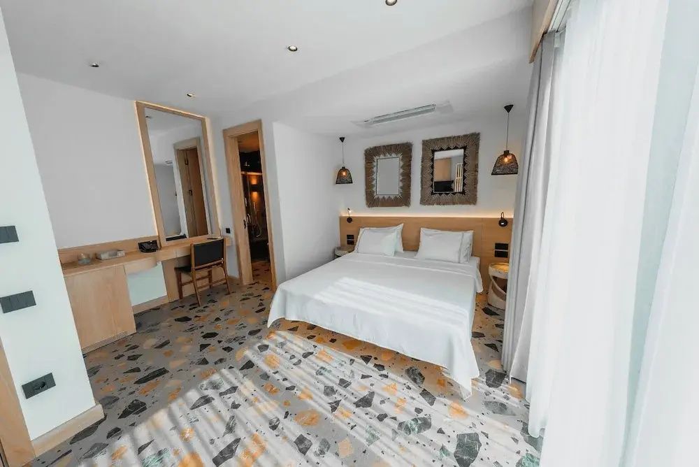 Hell eingerichtetes Schlafzimmer mit Doppelbett, Terrazzoboden und Schreibtisch.