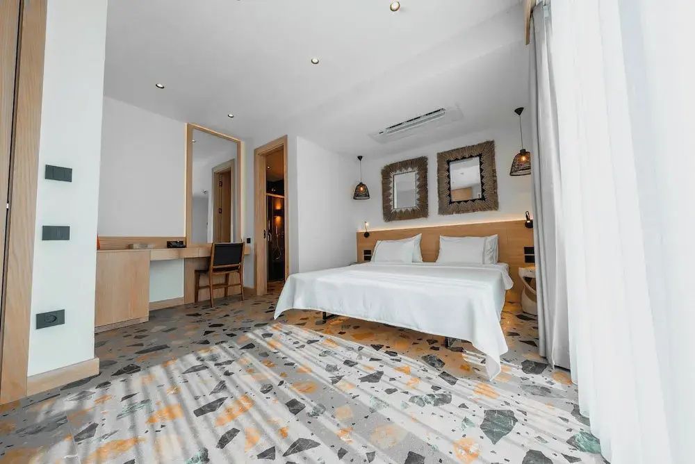Geräumiges Zimmer mit Doppelbett, Schreibtisch mit Stuhl und farbenfrohem Terrazzoboden.