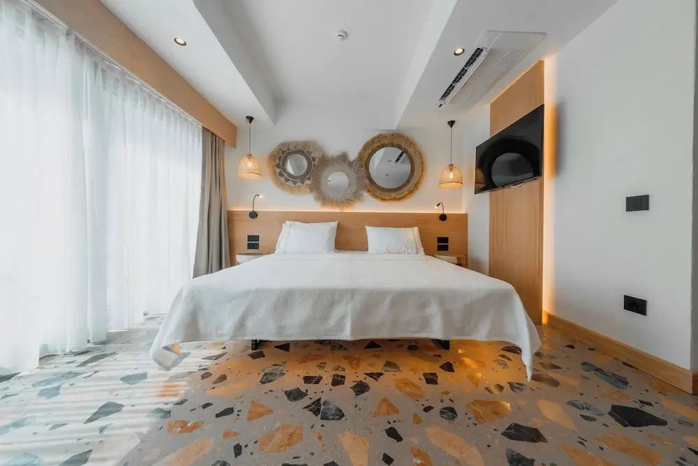 Frontalansicht des Doppelbetts im Zimmer mit Terrazzoboden und dekorativen Wandspiegeln.