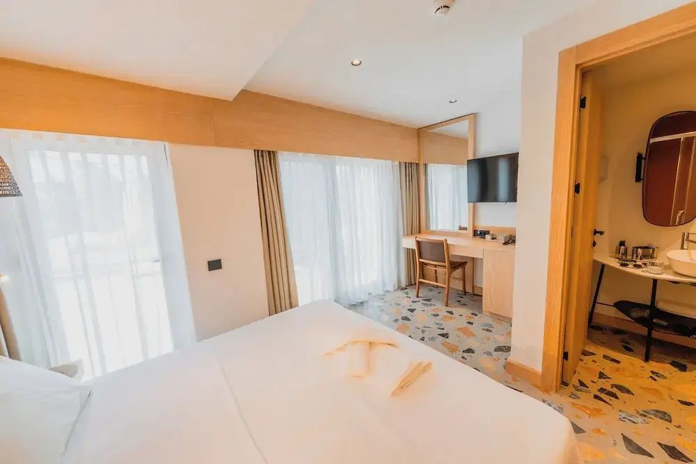 Hell eingerichtetes Hotelzimmer mit Schreibtisch, Fernseher und Bett.
