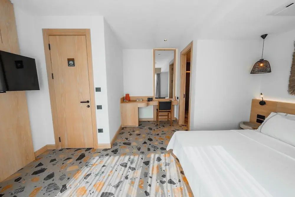 Arbeitsplatz und Eingangsbereich im Hotelzimmer mit Holztür und Terrazzoboden.
