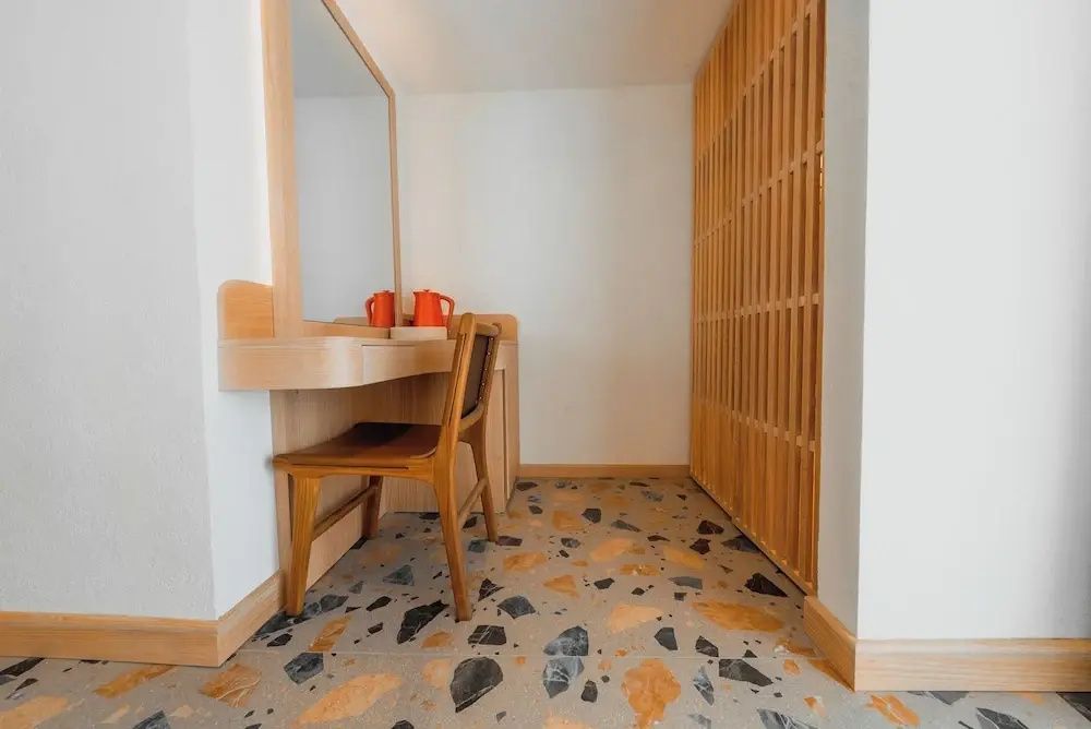 Schminktisch mit Holzstuhl, Wandspiegel und Holzverkleidung auf buntem Terrazzoboden.