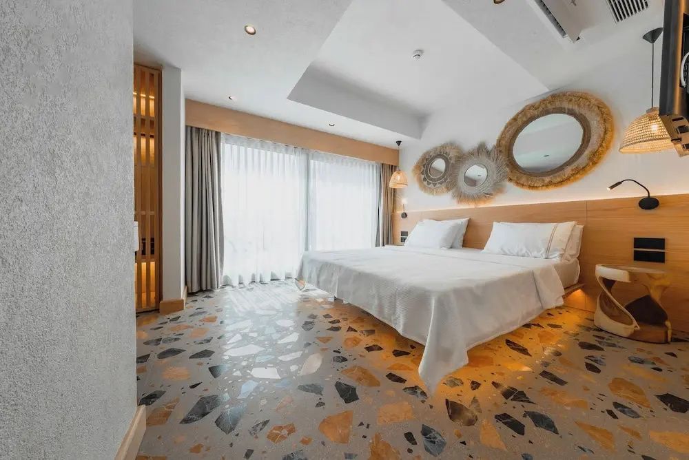 Geräumiges Zimmer mit Doppelbett, rundem Spiegelelement und großen Fenstern mit weißer Gardine.