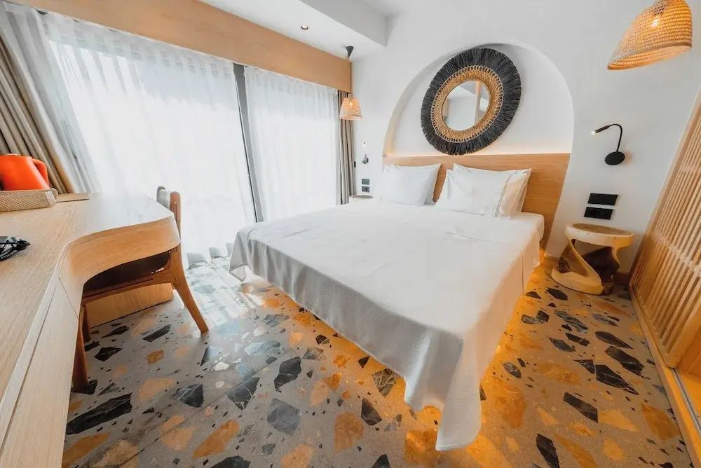 Hotelzimmer mit weiß bezogenem Doppelbett, Schreibtisch und rundem Wandspiegel.