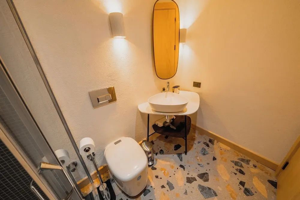 Badezimmer mit weißem Aufsatzwaschbecken, Toilette und ovalem Wandspiegel.
