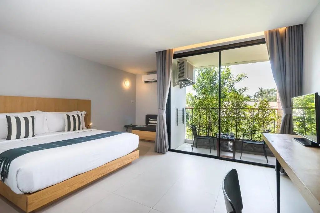 Helles Hotelzimmer mit Doppelbett, Sitzbereich und Balkontür mit Blick ins Grüne.