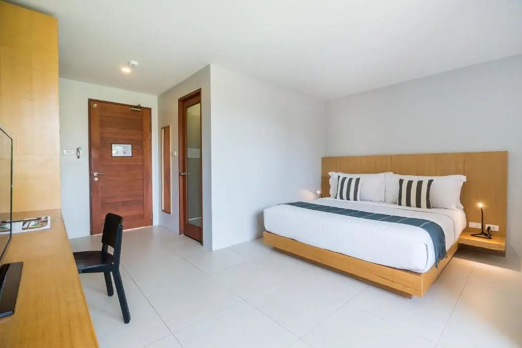Helles Zimmer mit Holzdoppelbett, weißer Bettwäsche und Holzeingangstür.