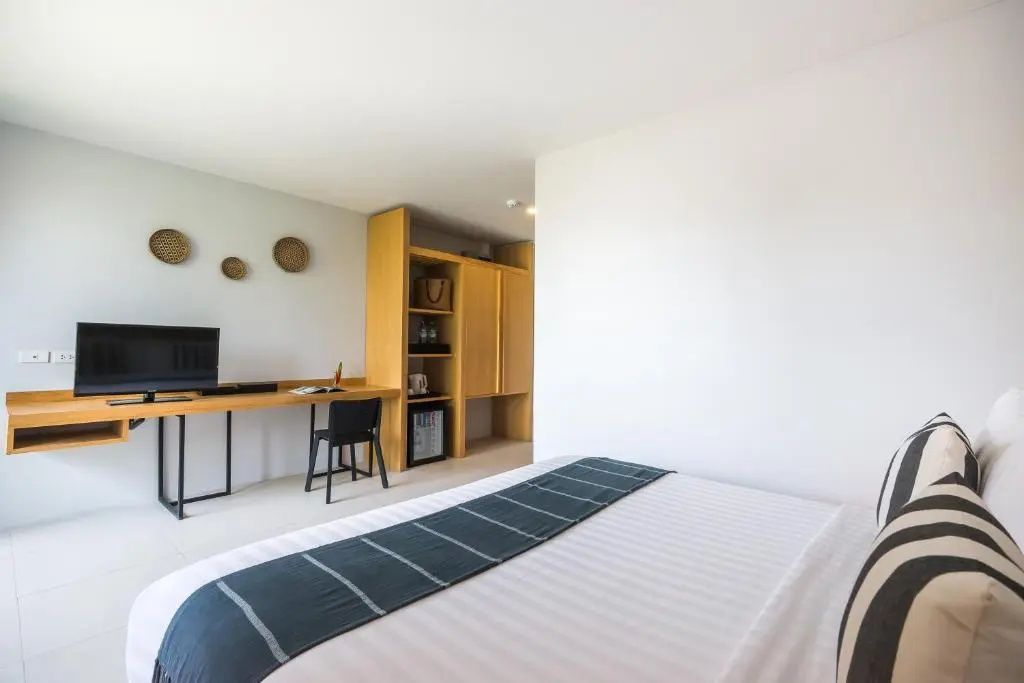 Blick vom Bett auf einen Schreibtisch aus Holz mit Fernseher und Schrank.