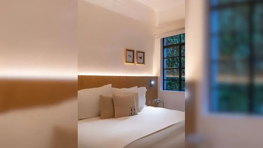 Modernes Hotelzimmer mit bezogenem Doppelbett, Holz Kopfteil mit Beleuchtung und Fenster.