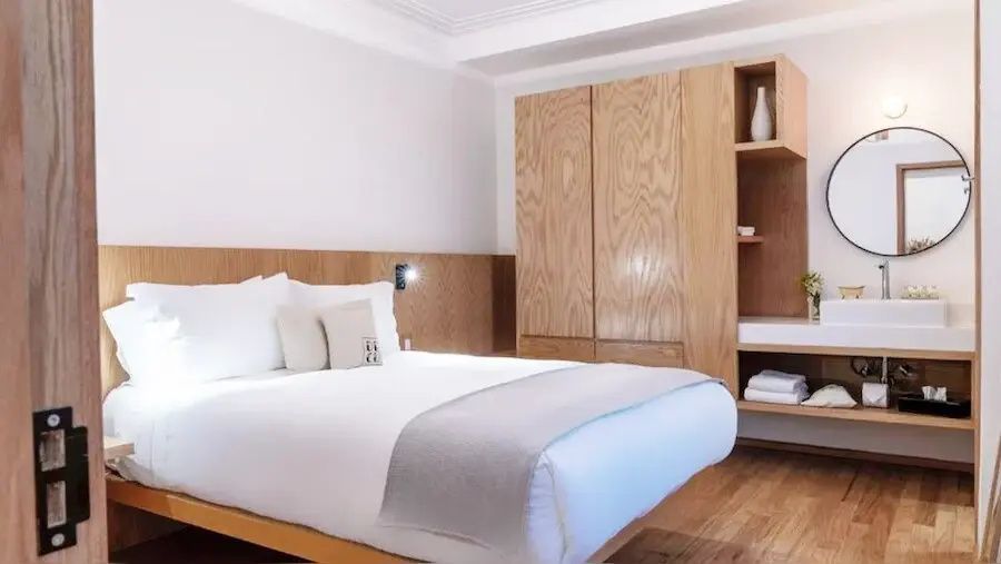Doppelbett mit weißer Bettwäsche und hellbraunem Kopfteil neben einem Holzschrank.