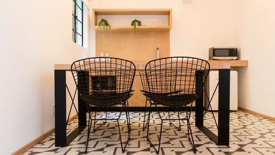 Zwei schwarze Metallstühle an einem Holztisch vor einer Wand mit Holzregal und Fliesenboden.