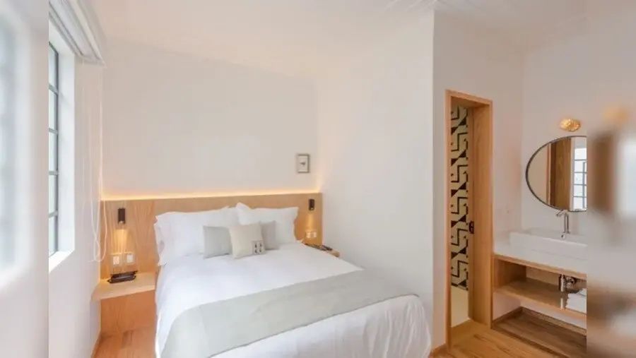 Helles Schlafzimmer mit bezogenem Doppelbett und beleuchteter Wand aus Holz.