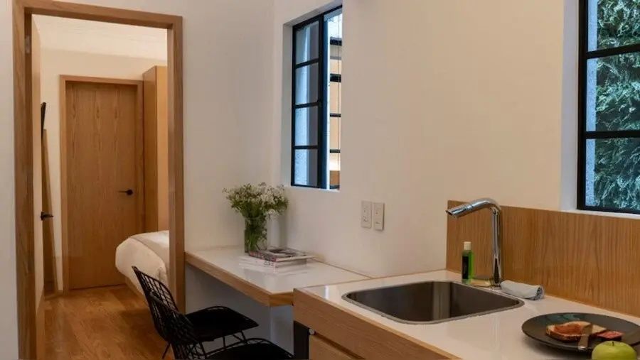 Küchenzeile und Arbeitsbereich im Hotelzimmer mit Spülbecken, Stuhl und Blumenstrauß.