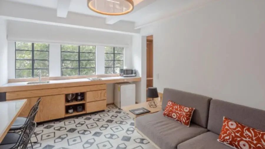 Wohnbereich einer Suite mit gemusterten Bodenfliesen, Sofa und Küchenzeile aus Holz.