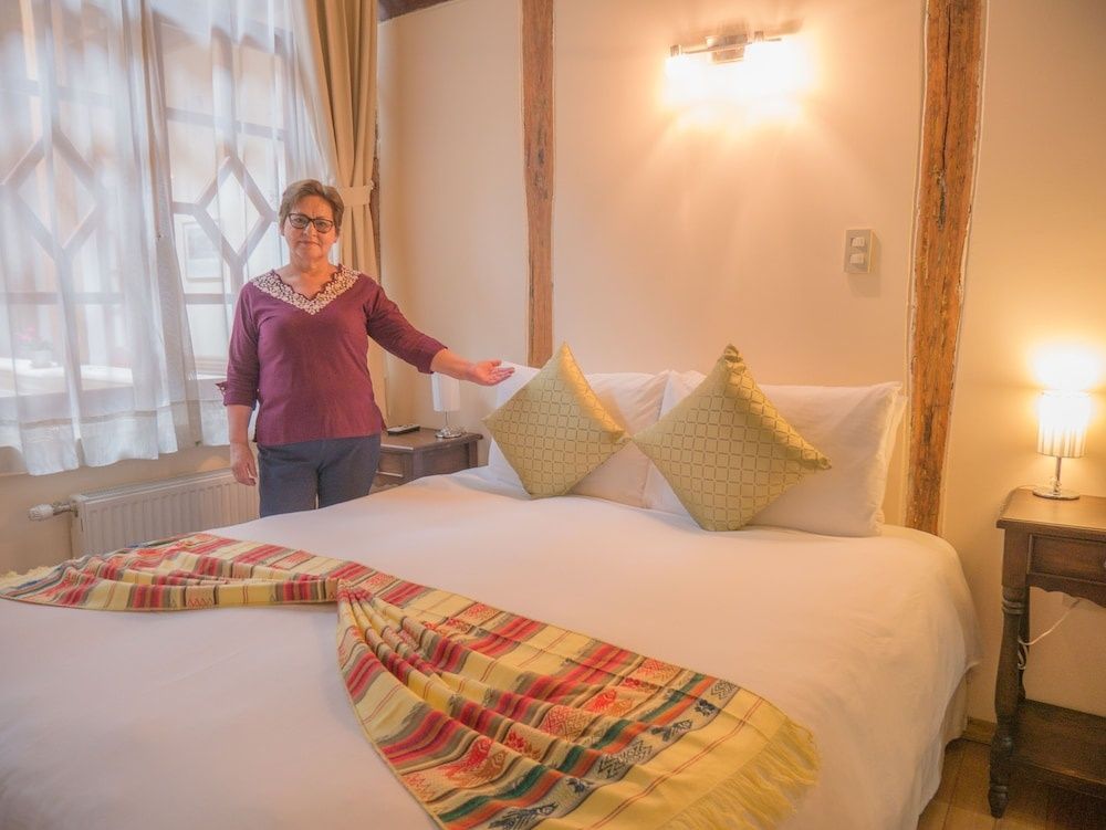Ein Doppelbett mit weißer Bettwäsche, zwei Zierkissen und buntem Schal in einem Hotelzimmer.