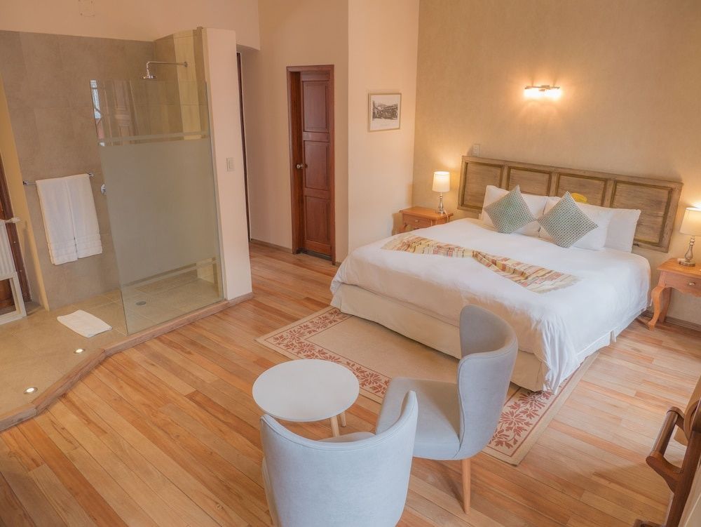 Großes Hotelzimmer mit Doppelbett, Sitzecke, Holzboden und offener Dusche.