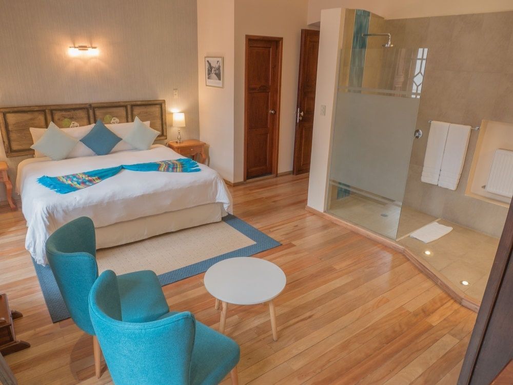 Hotelzimmer mit blauen Sesseln, Couchtisch, Doppelbett und begehbarer Dusche.