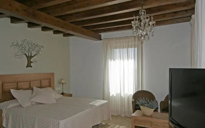 Schlafzimmer mit Holzbalkendecke, Doppelbett, Kristallkronleuchter und Gardinen.