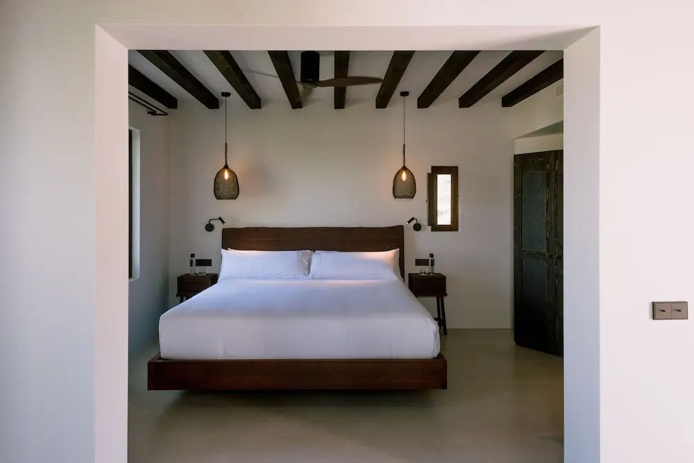 Blick in ein Schlafzimmer mit Holzdoppelbett, dunklen Holzbalken an der Decke und Hängeleuchten.