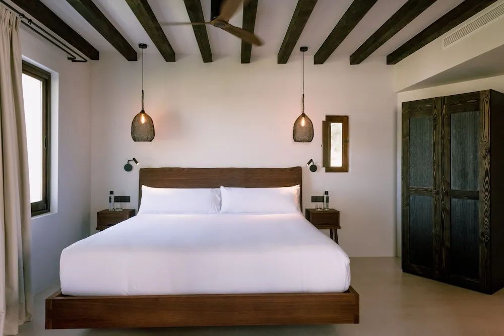 Helles Hotelzimmer mit großem Holzdoppelbett, Nachttischen und sichtbaren Holzbalken.