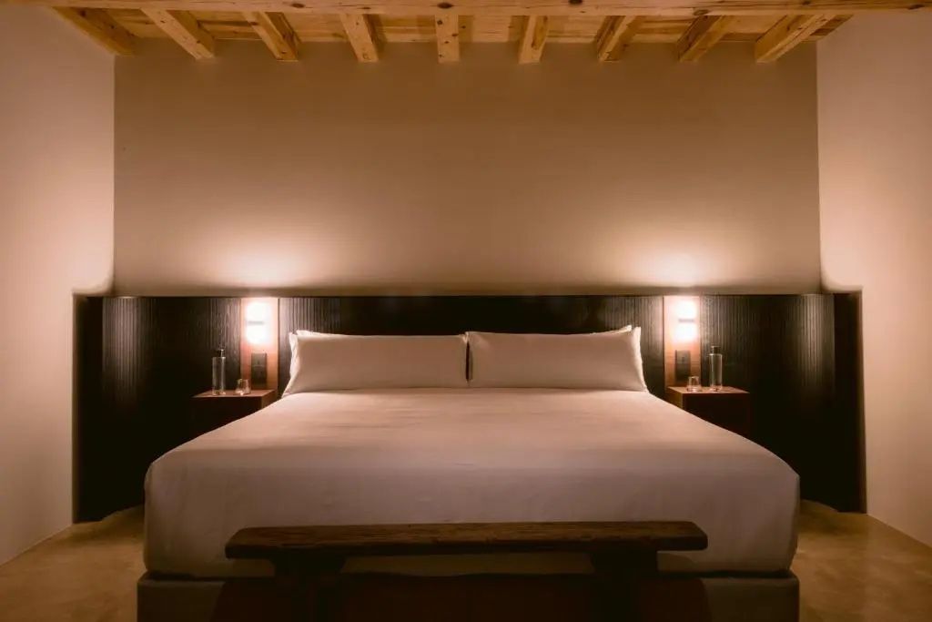 Großes Doppelbett mit weißer Bettwäsche, dunklem Kopfteil und Beleuchtung.