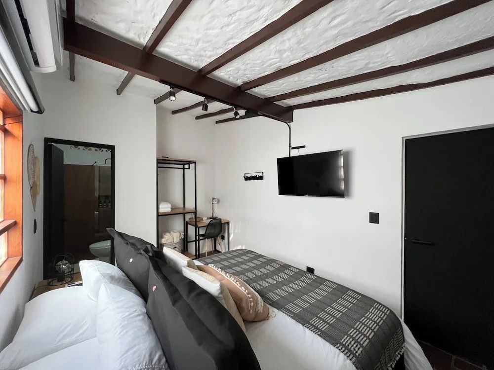 Schlafzimmer mit Doppelbett, dunklen Holzbalken an der Decke und Fernseher an der Wand.