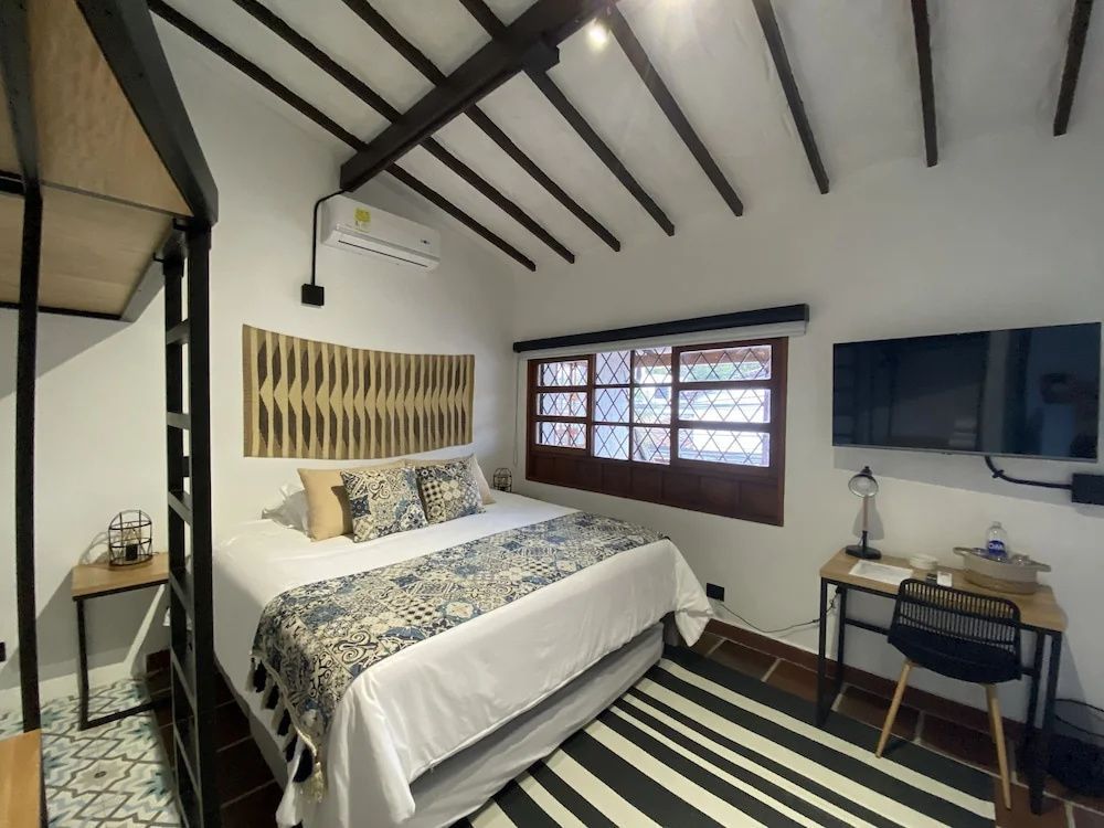 Hotelzimmer mit großem Doppelbett, Schreibtisch, Fernseher und Holzbalkendecke.