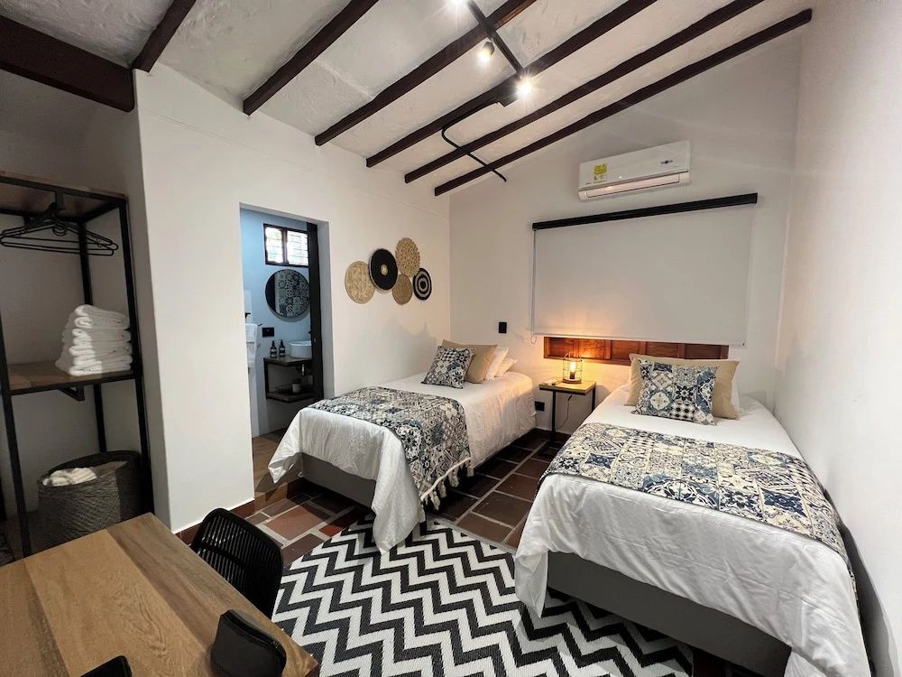 Zimmer mit zwei Einzelbetten, Schreibtisch, Fliesenboden und Blick ins Badezimmer.