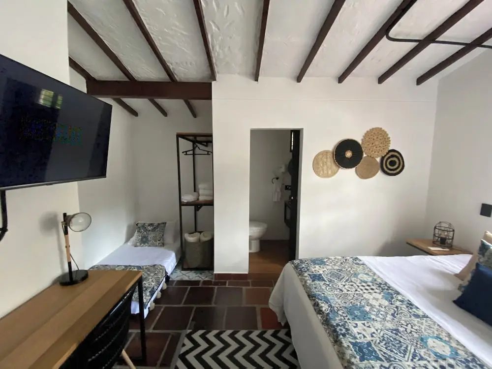 Helles Hotelzimmer mit Holzbalkendecke, Fliesenboden, zwei Betten und Schreibtisch.