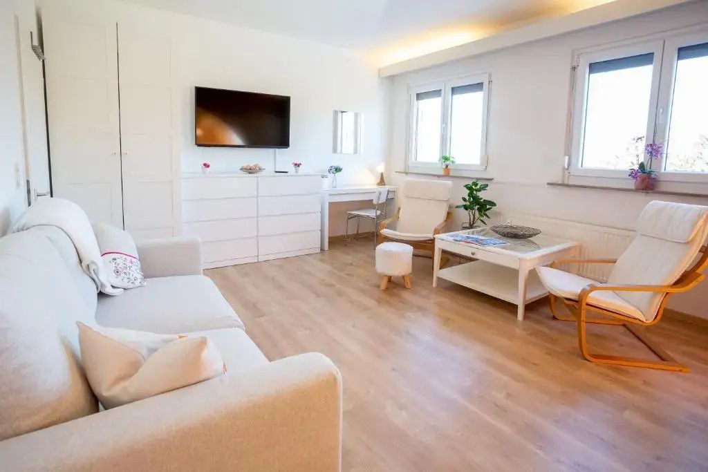 Heller Wohnbereich mit weißem Sofa, Fernseher an der Wand, Sessel und Couchtisch.