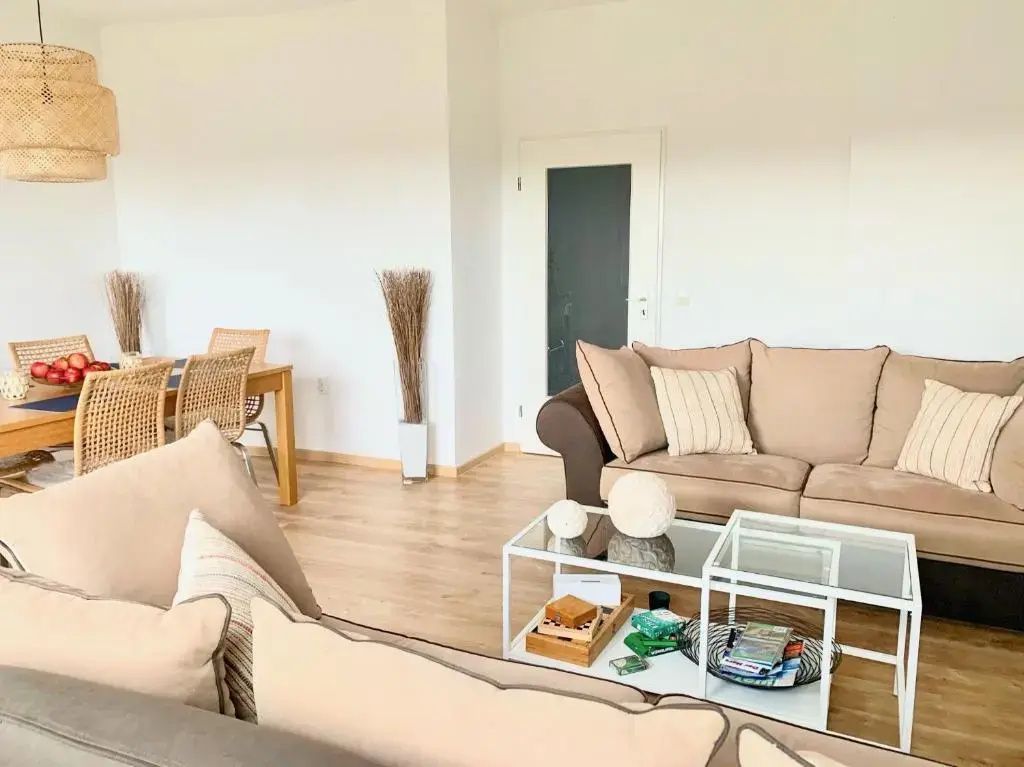 Moderner Wohnbereich mit beigem Sofa, Glascouchtisch auf Holzfußboden und weißer Tür.