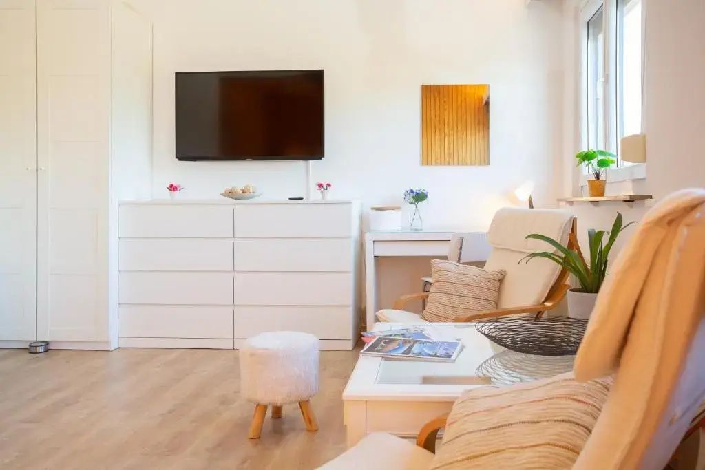 Sitzecke im Wohnbereich mit Fernseher über einer weißen Kommode und Beistelltisch.