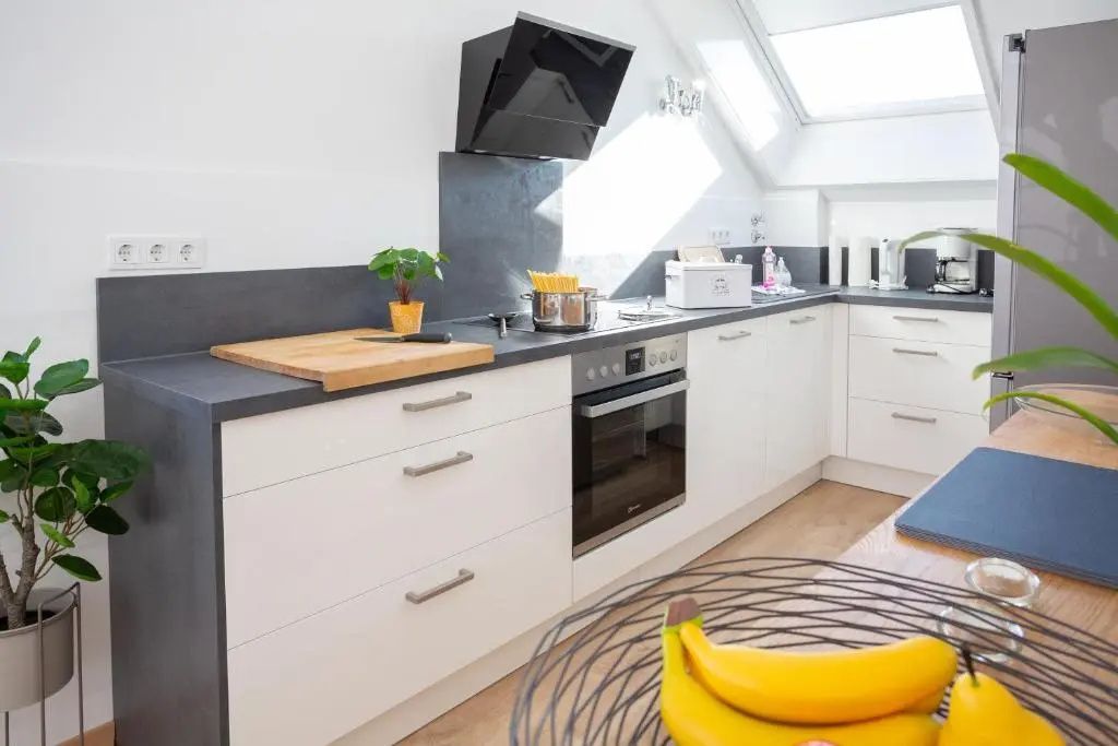 Moderne weiße Küche mit Backofen, Herdplatte, dunkler Arbeitsplatte und Dachfenster.