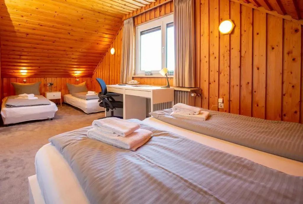 Schlafzimmer mit Holzverkleidung, zwei Einzelbetten, Schreibtisch und Fenster.