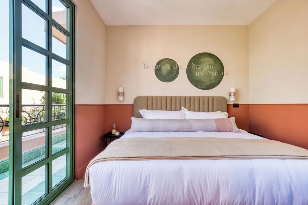 Helles Hotelzimmer mit großem Doppelbett, Wanddekoration und grünem Fensterrahmen.