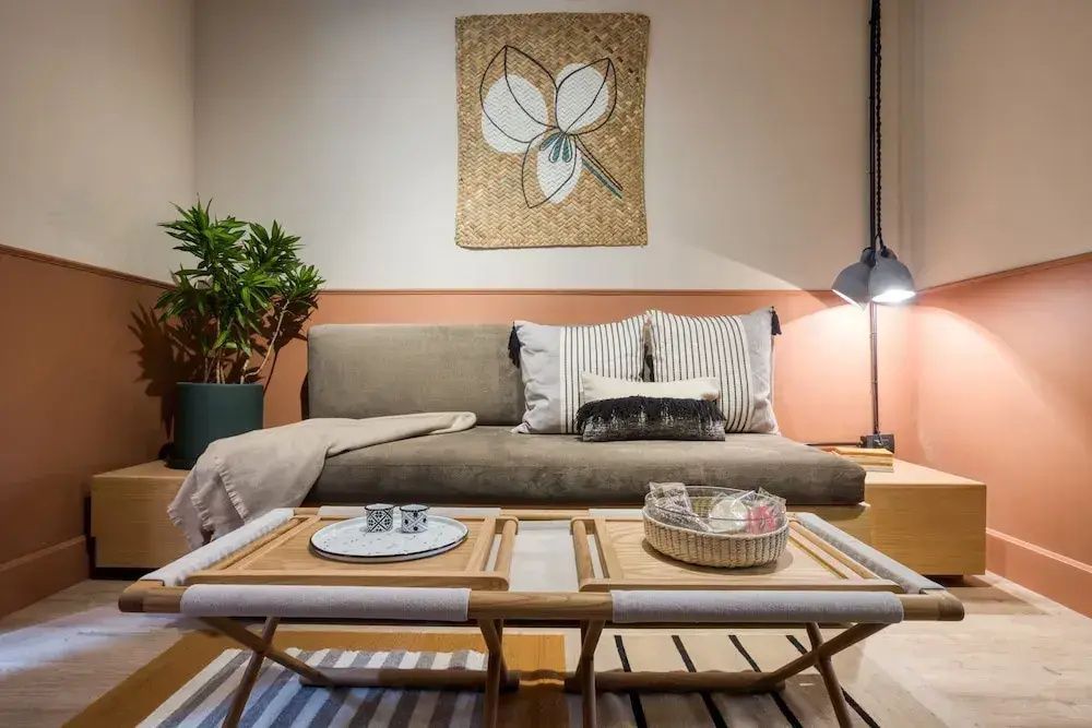 Sitzbereich mit braunem Sofa, Holzbeistelltischen und dekorativem Wandbehang.