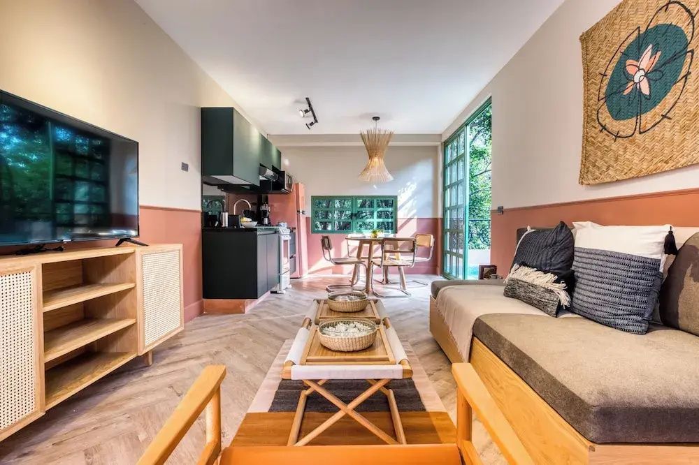 Offener Wohnbereich mit einer Küchenzeile, Sofa und Holztischen in warmen Erdtönen.