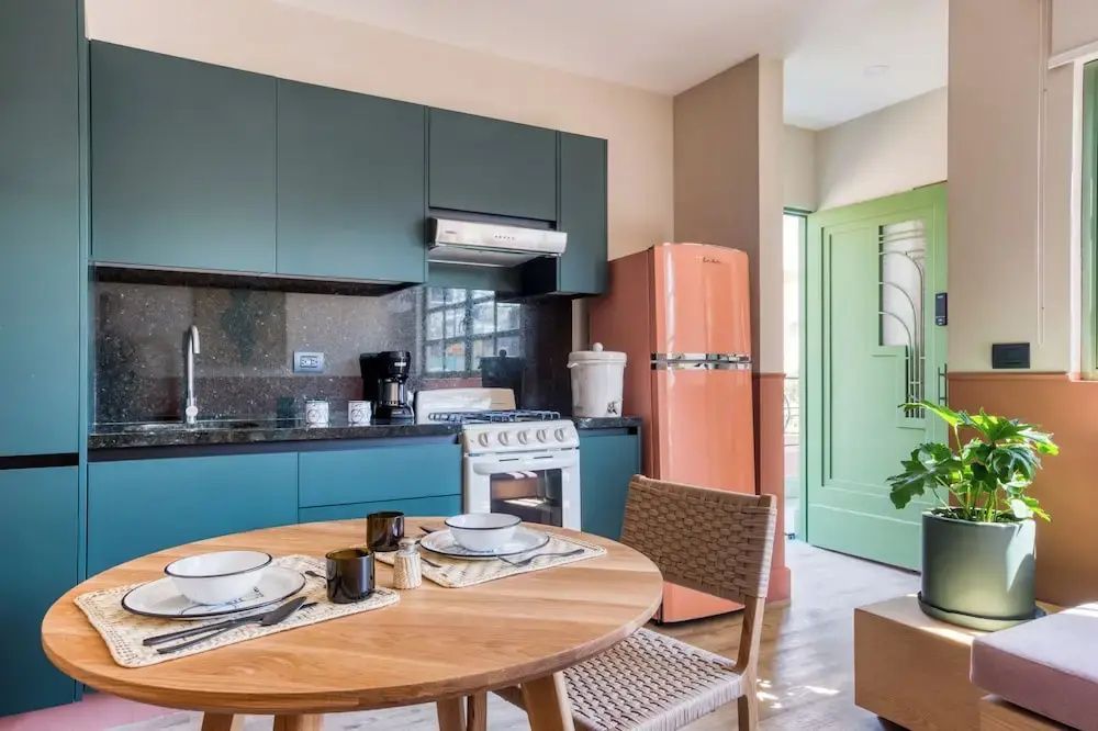 Küche mit dunkelblauen Fronten, einem orangefarbenen Kühlschrank und Holztisch.