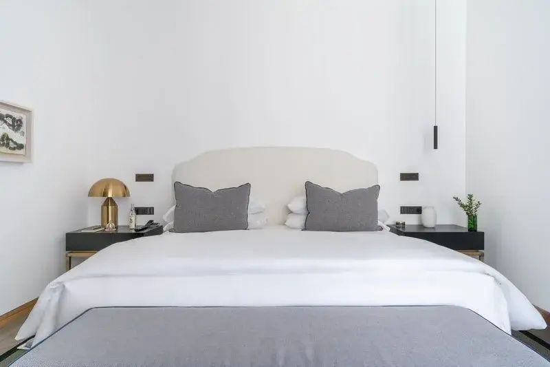 Doppelbett mit weißer Bettwäsche, grauen Kissen und zwei dunklen Nachttischen.