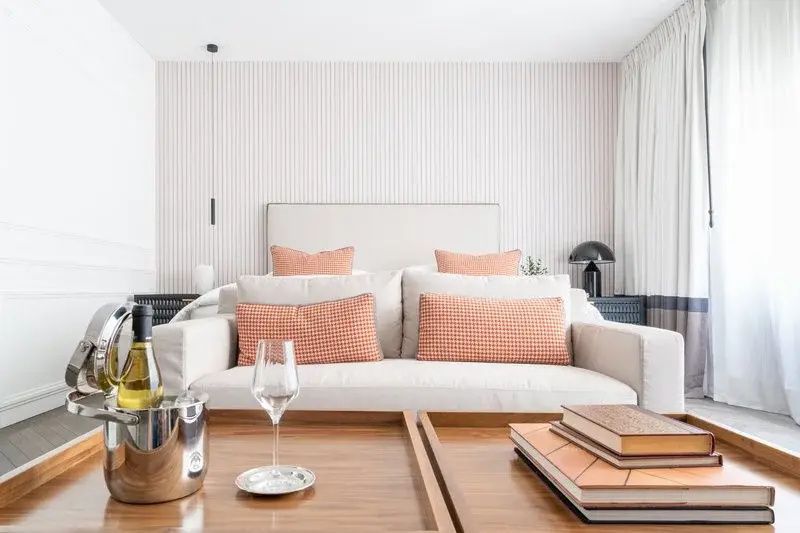 Sofa mit lachsfarbenen Kissen vor einem Bett, auf dem Holztisch stehen Gläser und Bücher.