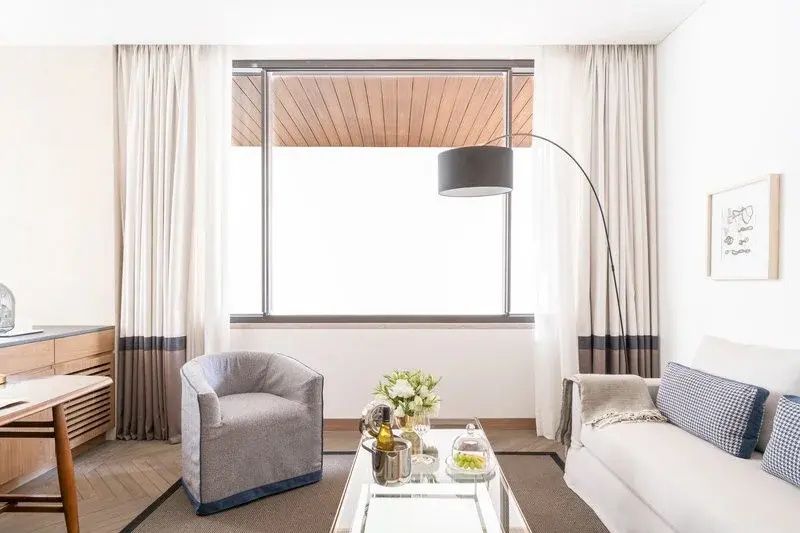 Heller Wohnbereich mit grauem Sessel, Stehlampe und Tisch vor großem Fenster.
