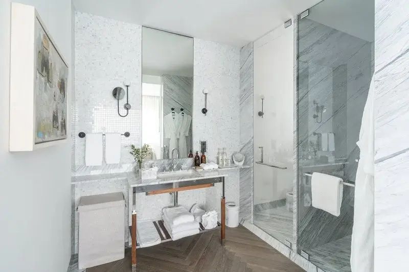 Marmorbadezimmer mit Waschtisch, großem Spiegel und verglaster Dusche mit Regenkopf.