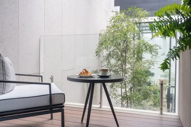Balkon mit kleinem Tisch, Kaffee und Croissant vor einer Glasbrüstung und Pflanzen.